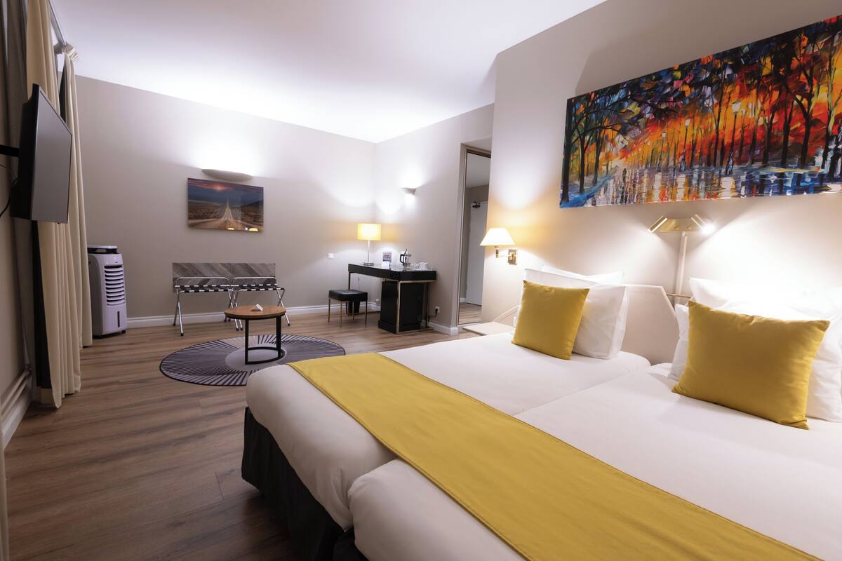 Habitación de hotel con una cama grande, un escritorio, una silla, un televisor y obras de arte en las paredes.