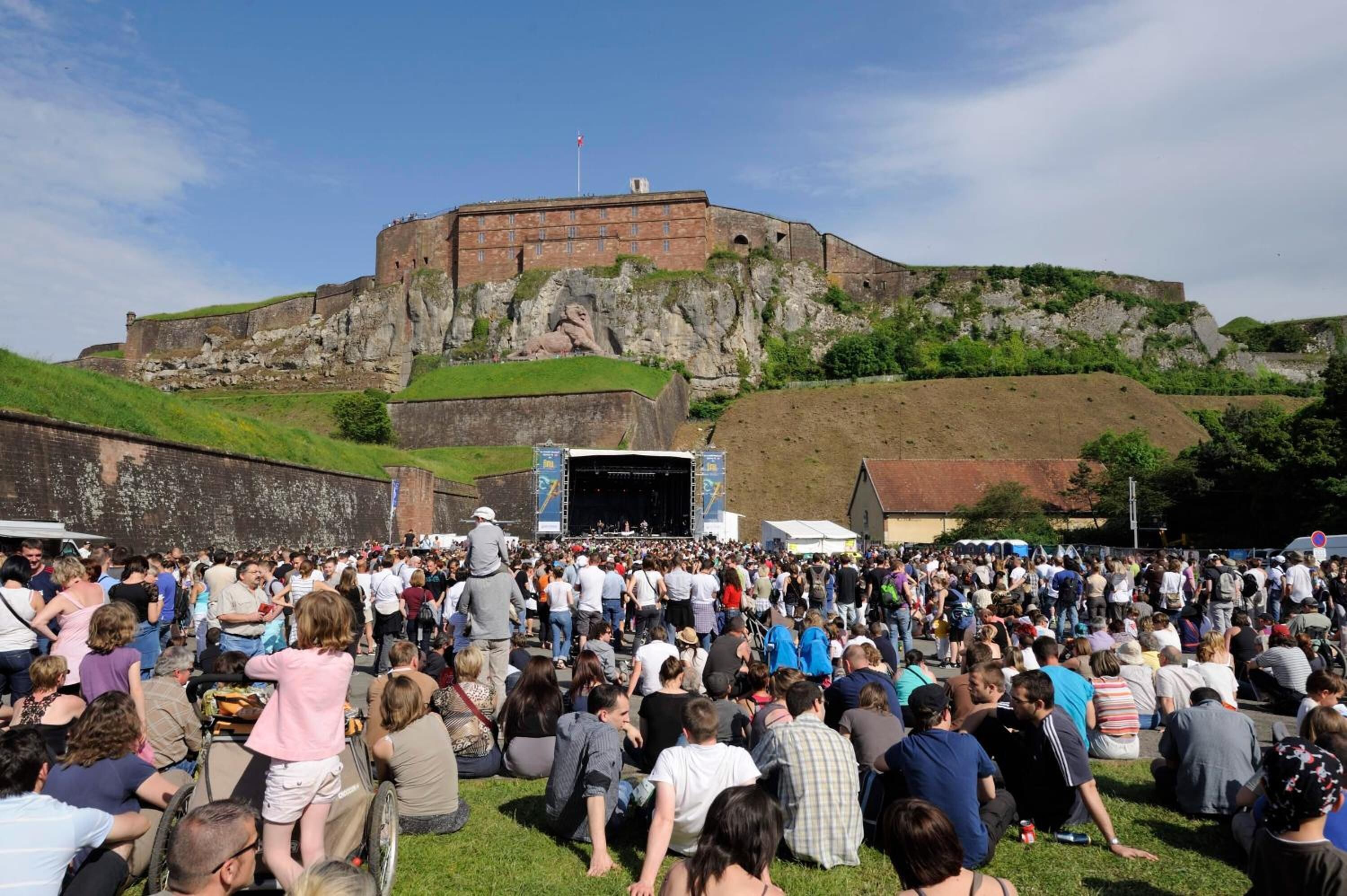 A crowd gathered in an open area with a stage and a fort-like structure in the background.