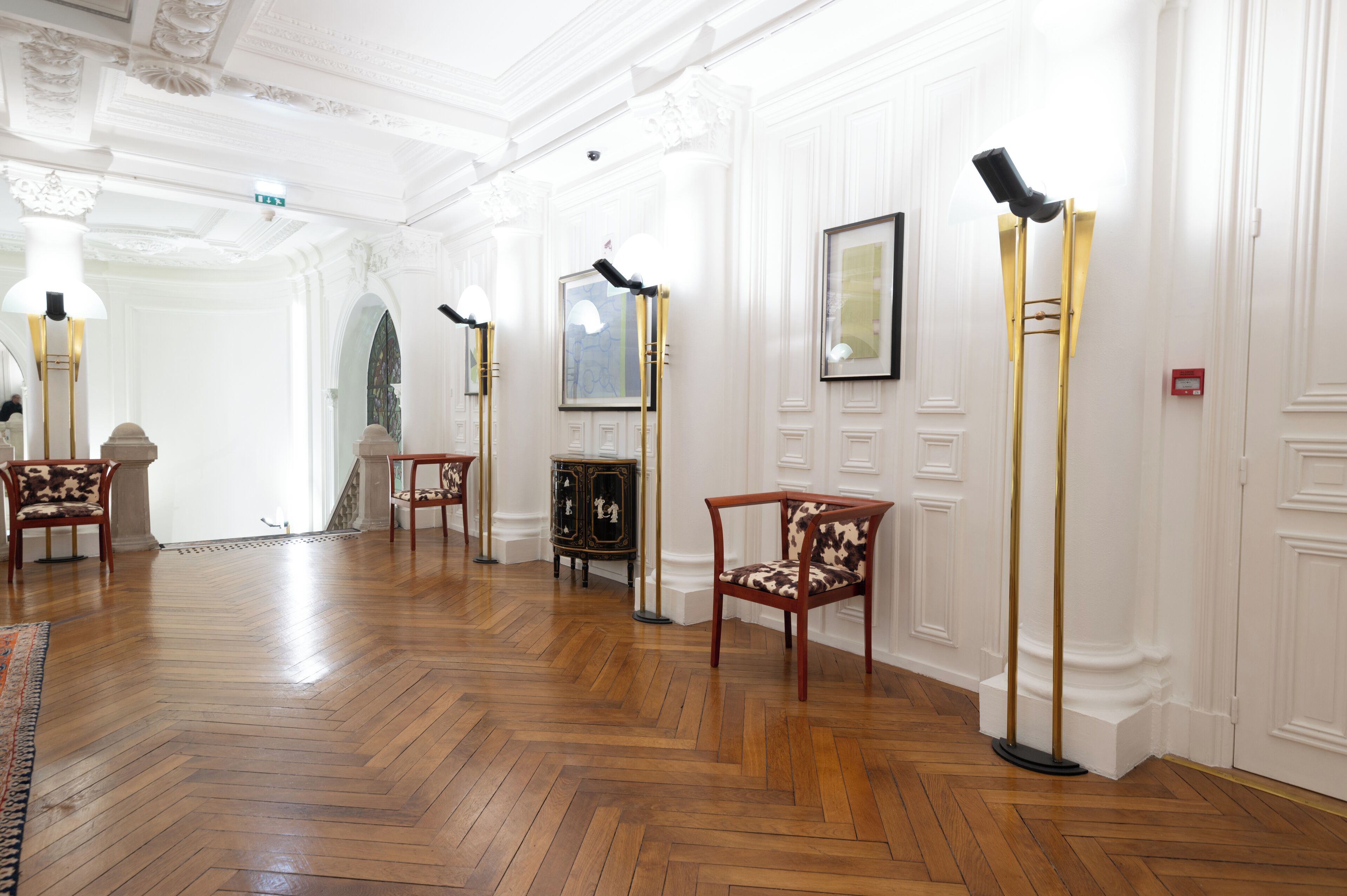 A hallway with wooden flooring, white walls, and a series of framed pictures and floor lamps.
