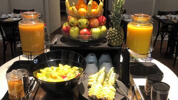 Een buffettafel met een fruitpresentatie in drie verdiepingen, een schaal met ananasstukjes en twee kannen jus d'orange.