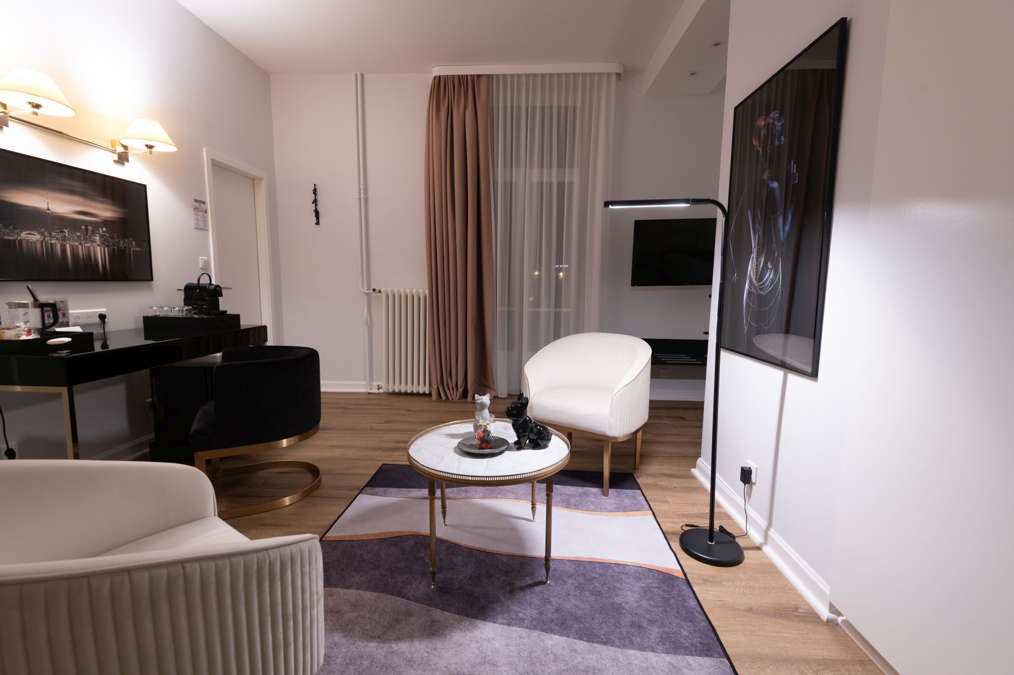 A modern living room with a round coffee table, a white armchair, a black sofa, a black TV stand, and a large painting on the wall.