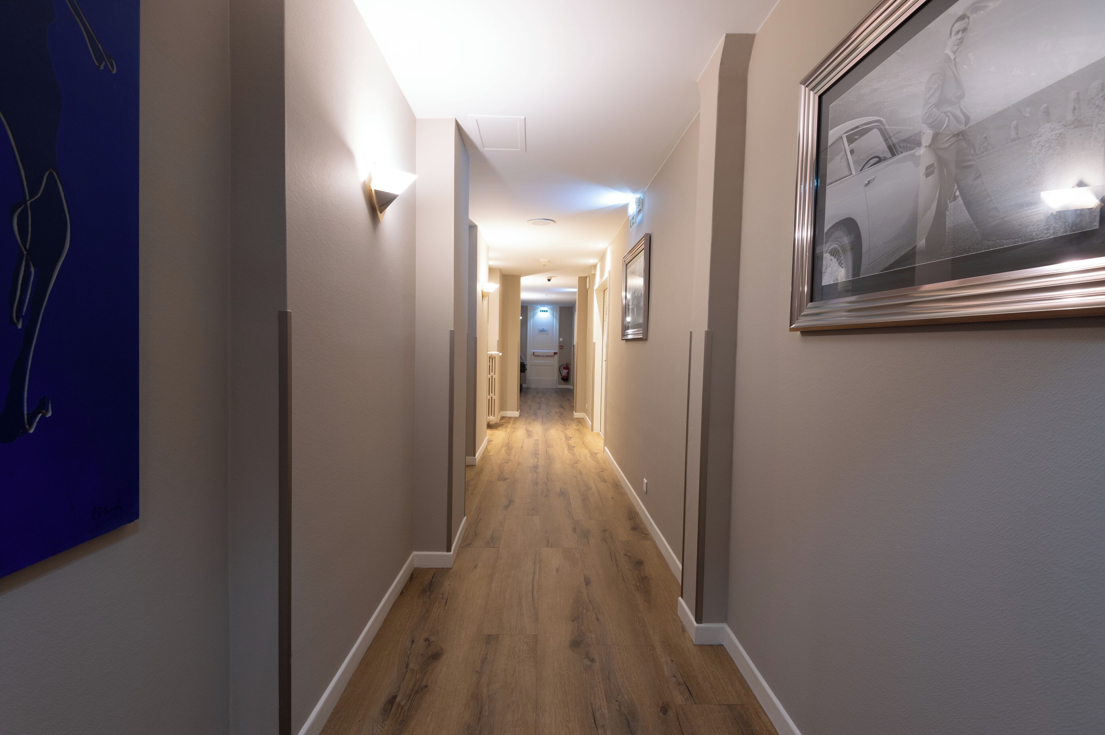 A hallway with a wooden floor, light-colored walls, and framed artwork on the walls.