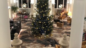 Um saguão imponente com uma grande árvore de Natal, colunas ricamente decoradas e um tapete estampado.