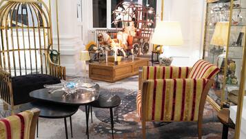 A cozy living room with a wooden coffee table, striped armchairs, a glass cabinet, and a decorative horse carriage.