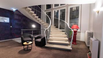 A modern hotel lobby with a curved staircase, a red lamp, a black armchair, and a small table.