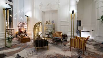 A luxurious interior with ornate white walls, a patterned carpet, and elegant furniture including a gold chair, a striped sofa, and a glass display cabinet.