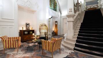 Een statige lobby met een trap, versierde wanddecoraties en een zithoek met gestreepte stoelen.