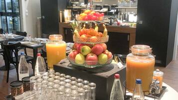 A buffet setup with a fruit display, beverage dispensers, and a clock on the wall.