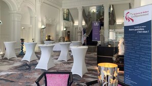 Um salão imponente com colunas brancas ricamente decoradas, um candelabro e mesas montadas para um evento formal.