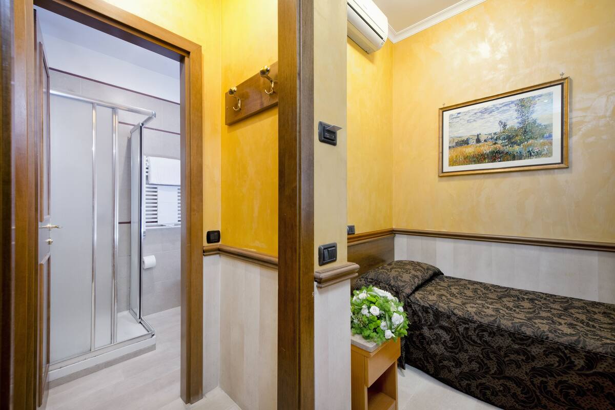 A hotel room with a shower, a bed with a floral arrangement, and a painting on the wall.