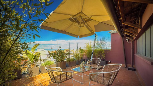 A patio with a table and chairs, an umbrella, and potted plants. - Hotel Marco Polo (Rome)