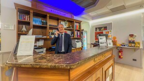 A reception desk with a marble top, wooden shelving with books and binders, a clock, and a fire extinguisher. - Hotel Marco Polo (Rome)