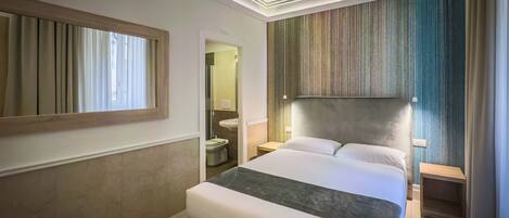A hotel room with a large bed, a bedside table, a mirror, and a view of the bathroom.