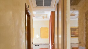 A hotel corridor with marble flooring, a bed with a red bedspread, and a door with a brass handle. - Hotel Marco Polo (Rome)