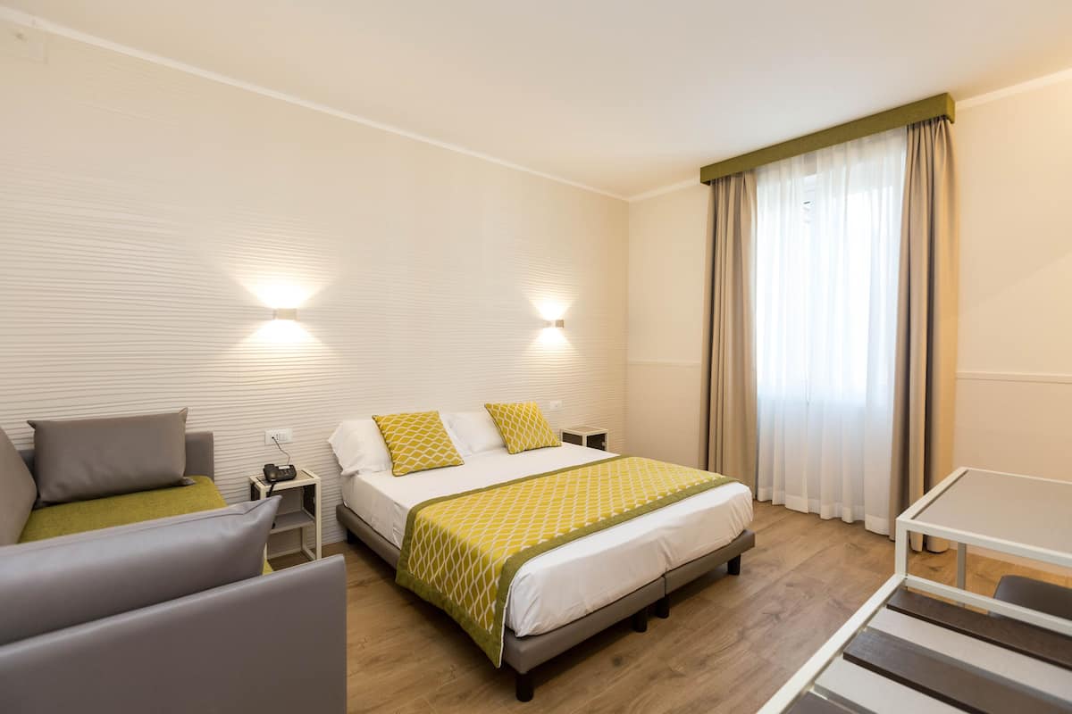 A modern hotel room with a bed, a sofa, a small table, and a nightstand.