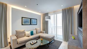 Een moderne woonkamer met een hoekbank, een glazen salontafel en een flatscreen televisie aan de muur.