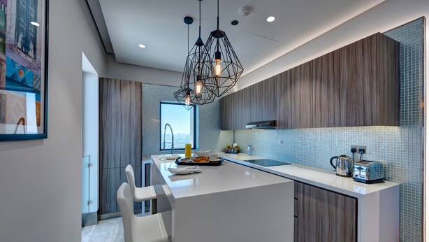 A modern kitchen with a central island, pendant lighting, and a view of the city. - Arjaan by Rotana Dubai Media City (Dubai)
