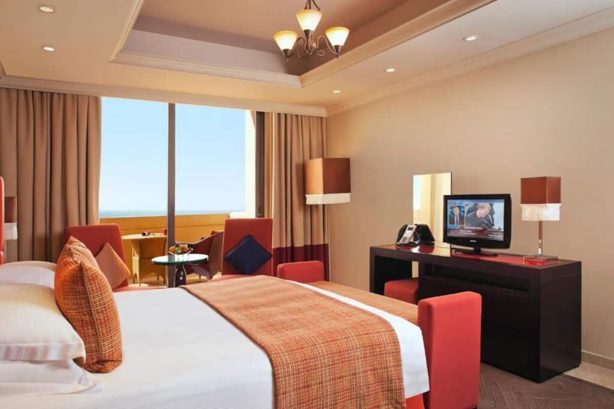 A hotel room with a large bed, a desk with a TV, and a view of the ocean.