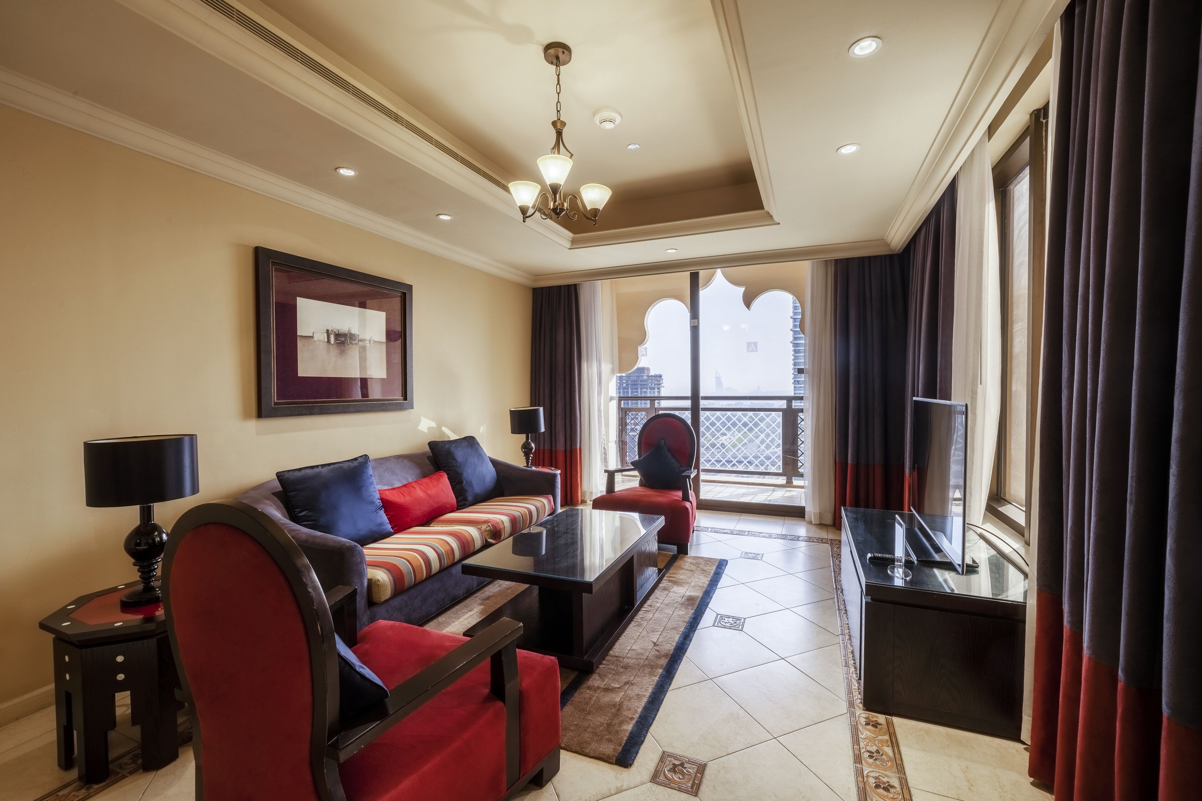 A hotel room with a sofa, a coffee table, a TV, and a balcony with curtains.