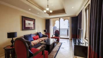 A hotel room with a sofa, a coffee table, a TV, and a balcony with curtains.