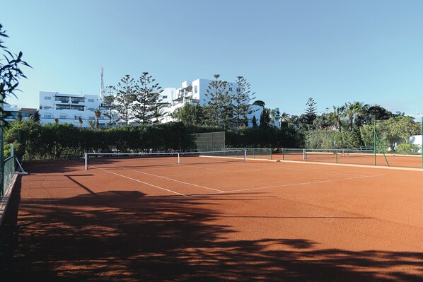 A tennis court with a net, surrounded by trees and buildings. - Hotel Riu Tikida Beach - Adults Only - All inclusive (Agadir)