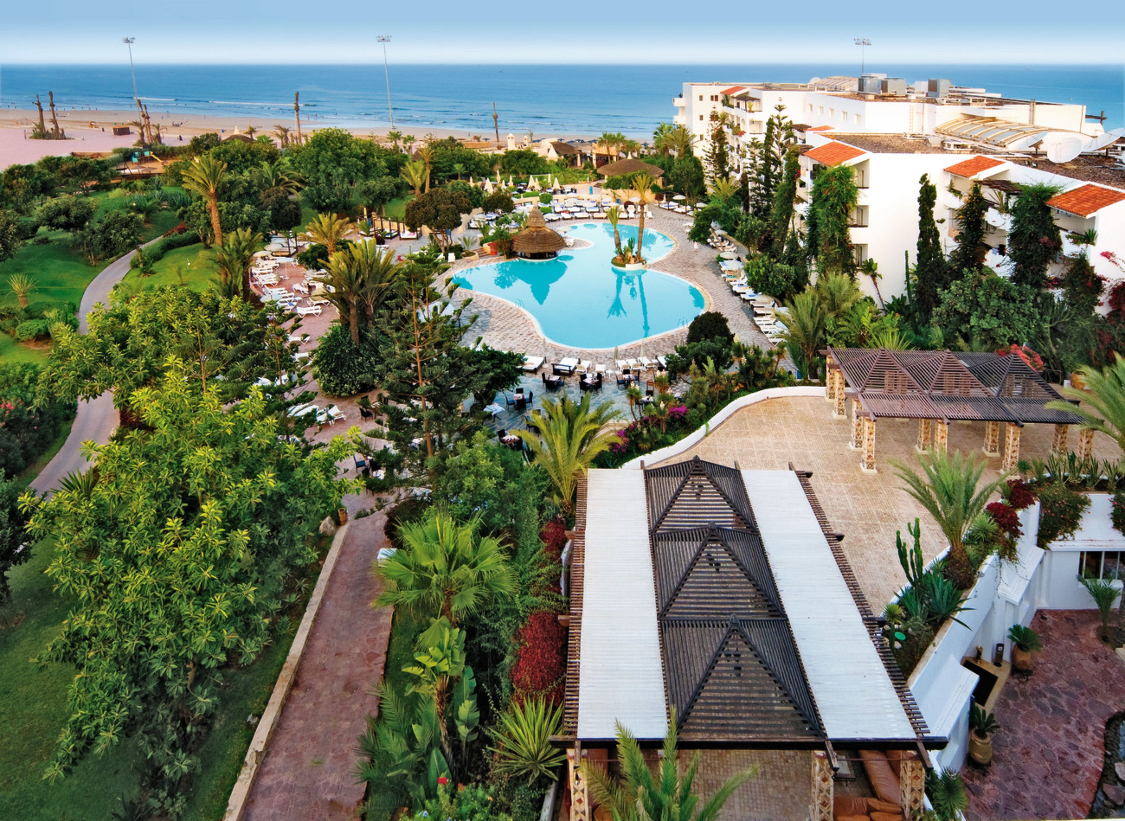 A resort with a central pool, lush greenery, and a view of the sea.