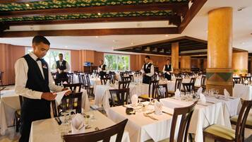 A restaurant with multiple tables set for dining, a waiter attending to a table, and a large pillar in the center.