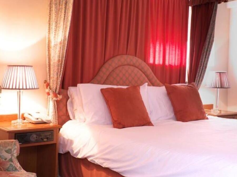 A hotel room with a bed, two bedside tables, a lamp, and curtains.
