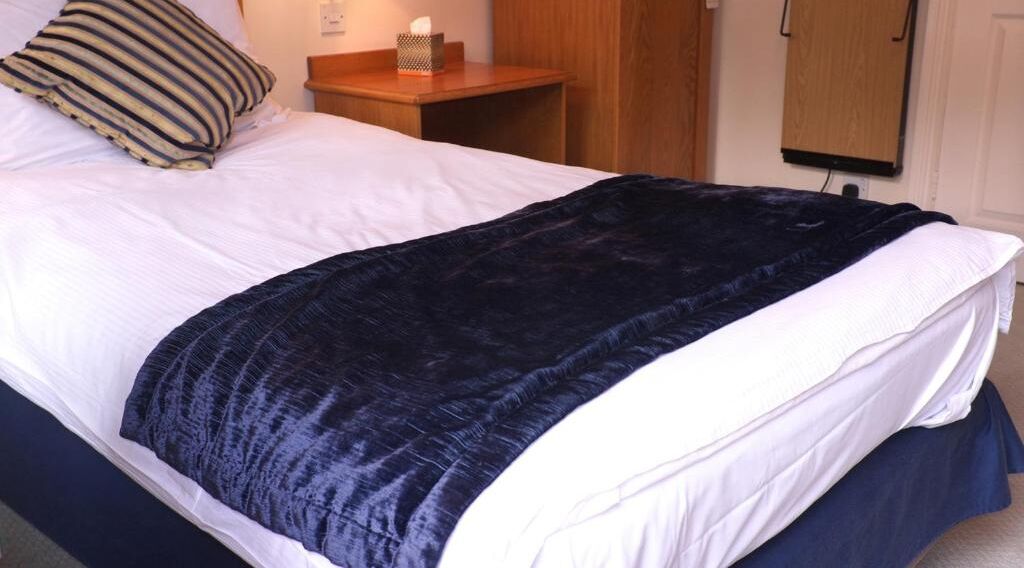 A neatly made bed with a dark blue blanket and a striped pillow.