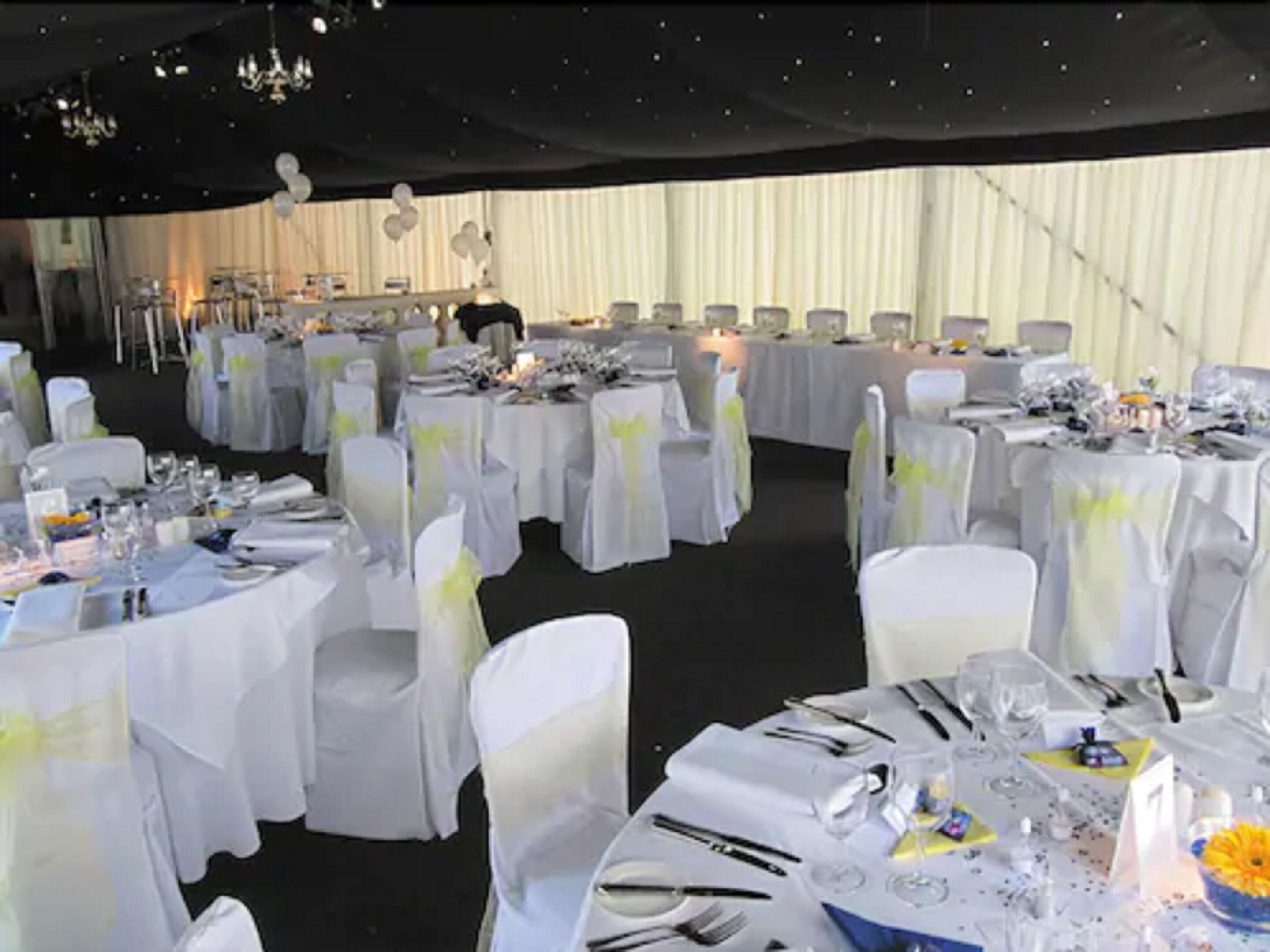 A banquet hall with round tables covered in white tablecloths and chairs with white and yellow sashes.