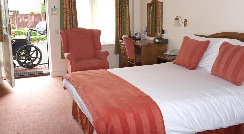 A hotel room with a large bed, a desk, a chair, and a wheelchair outside the door.