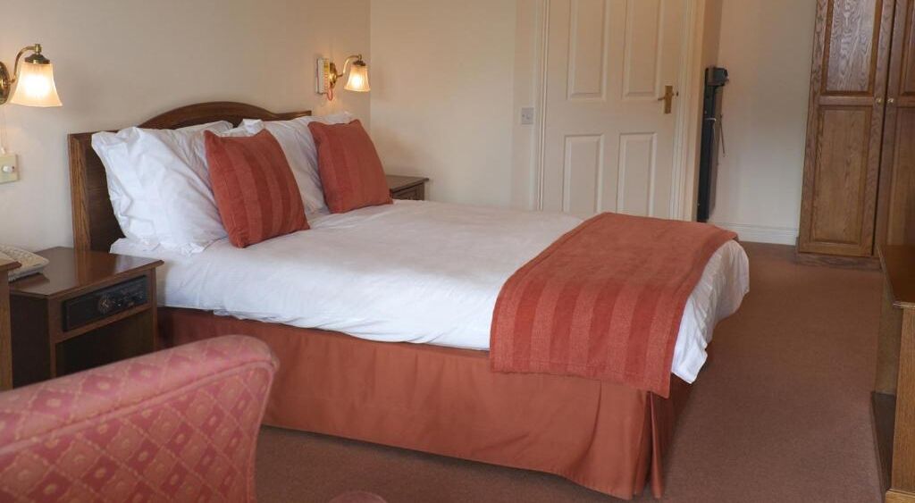 A neatly made bed with white and red bedding, a bedside table with a lamp, and a wooden wardrobe.
