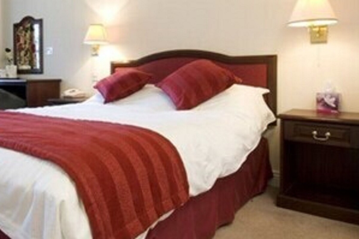 A neatly made bed with a red and white bedspread, a wooden headboard, and a nightstand with a lamp and a small drawer.