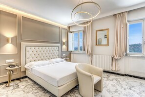 A hotel room with a large bed, a chair, a bedside table, a mirror, and a view of the city through the window. - Hotel Castel Vecchio (Castel Gandolfo)