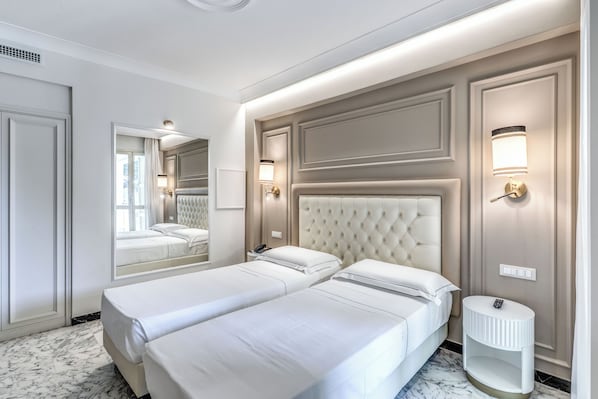 A hotel room with two beds, a large mirror, and wall-mounted lighting.
