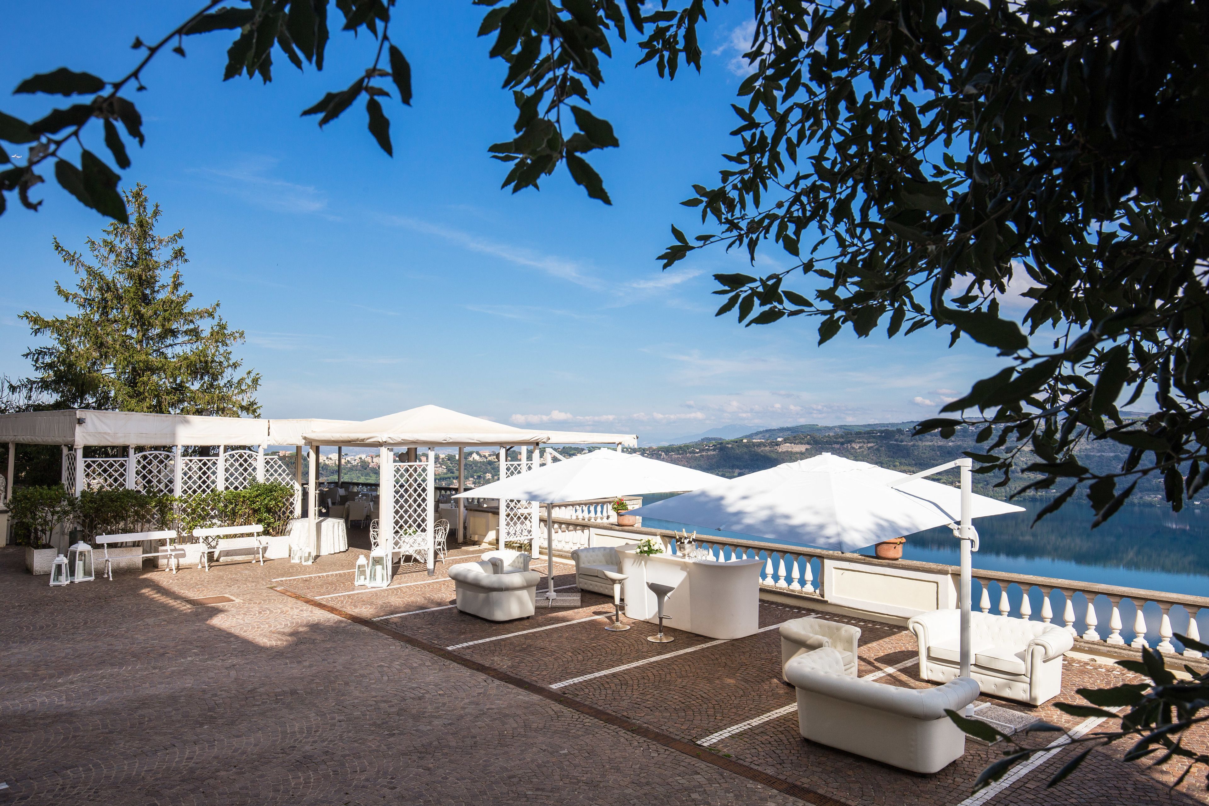 An outdoor terrace with white furniture, umbrellas, and a view of a lake.