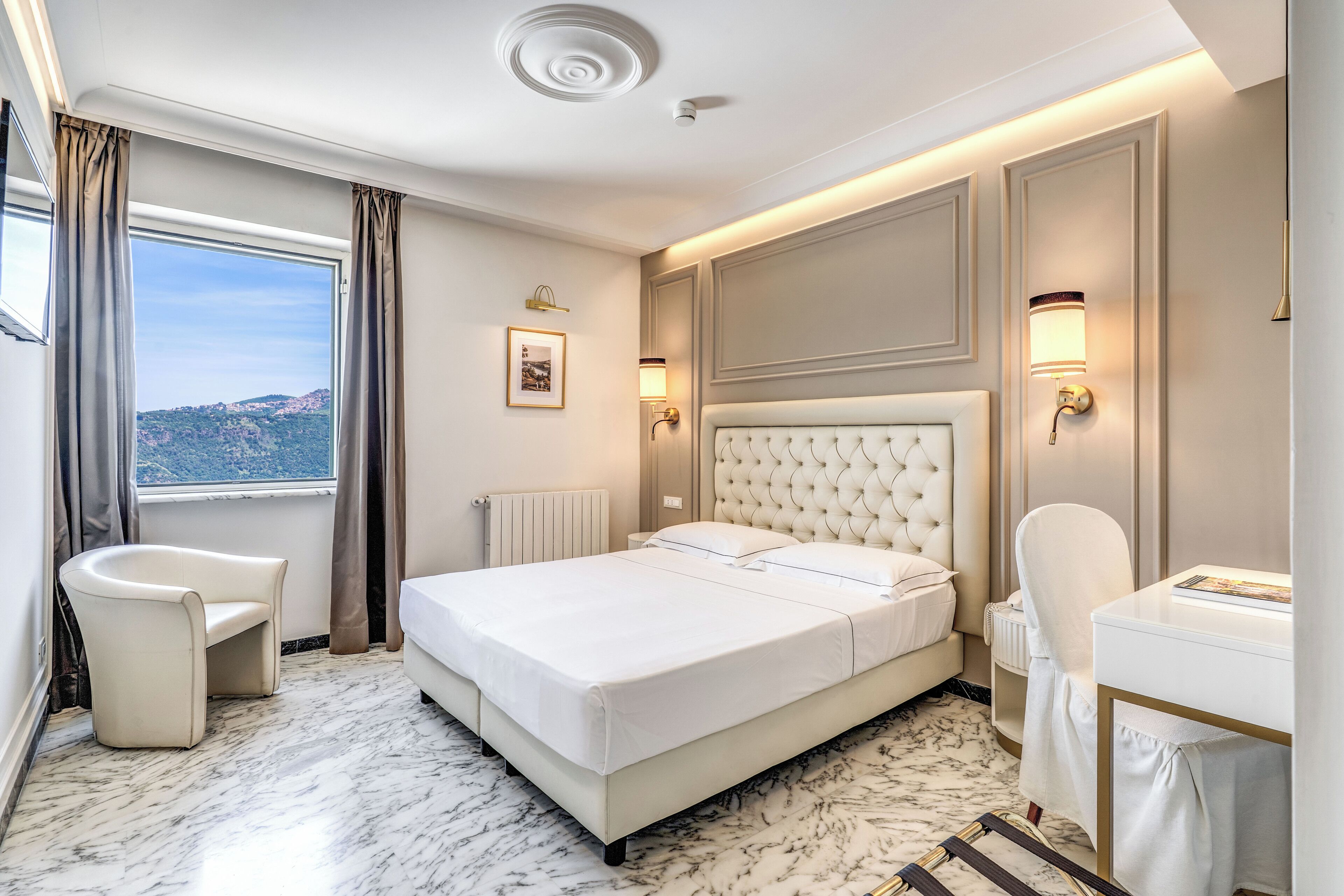 Ett hotellrum med en stor säng, en sittgrupp med en fåtölj, ett skrivbord och utsikt över bergen.