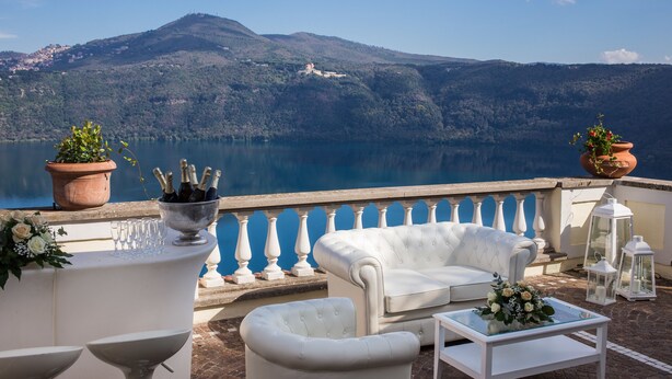 Una terrazza con arredi bianchi, vista su un lago e montagne sullo sfondo.