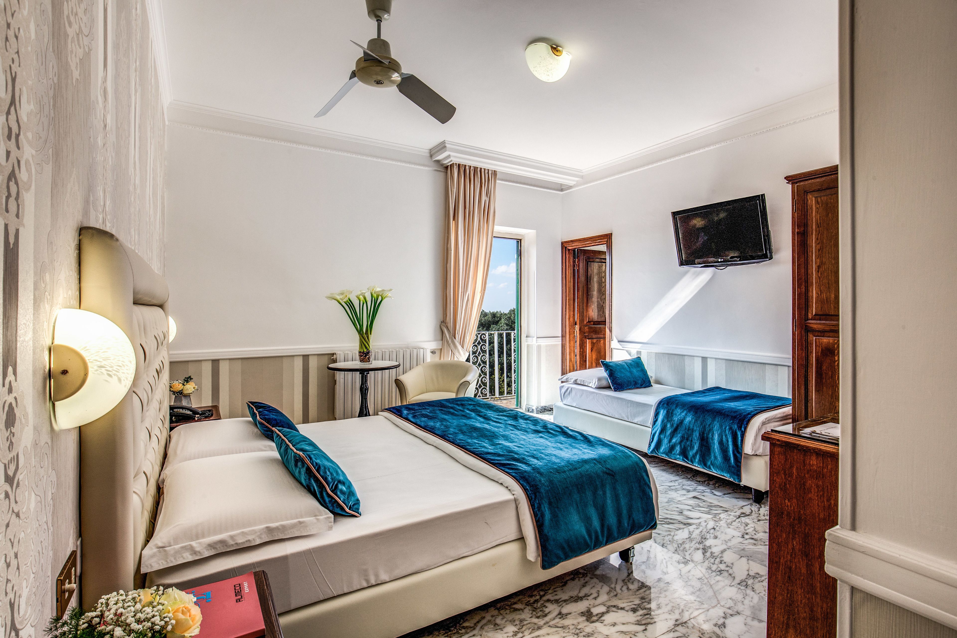 Habitación de hotel con dos camas, un ventilador de techo, televisión, una mesita con una planta y vistas al exterior.
