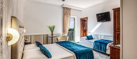Habitación de hotel con dos camas, un ventilador de techo, televisión, una mesita con una planta y vistas al exterior.