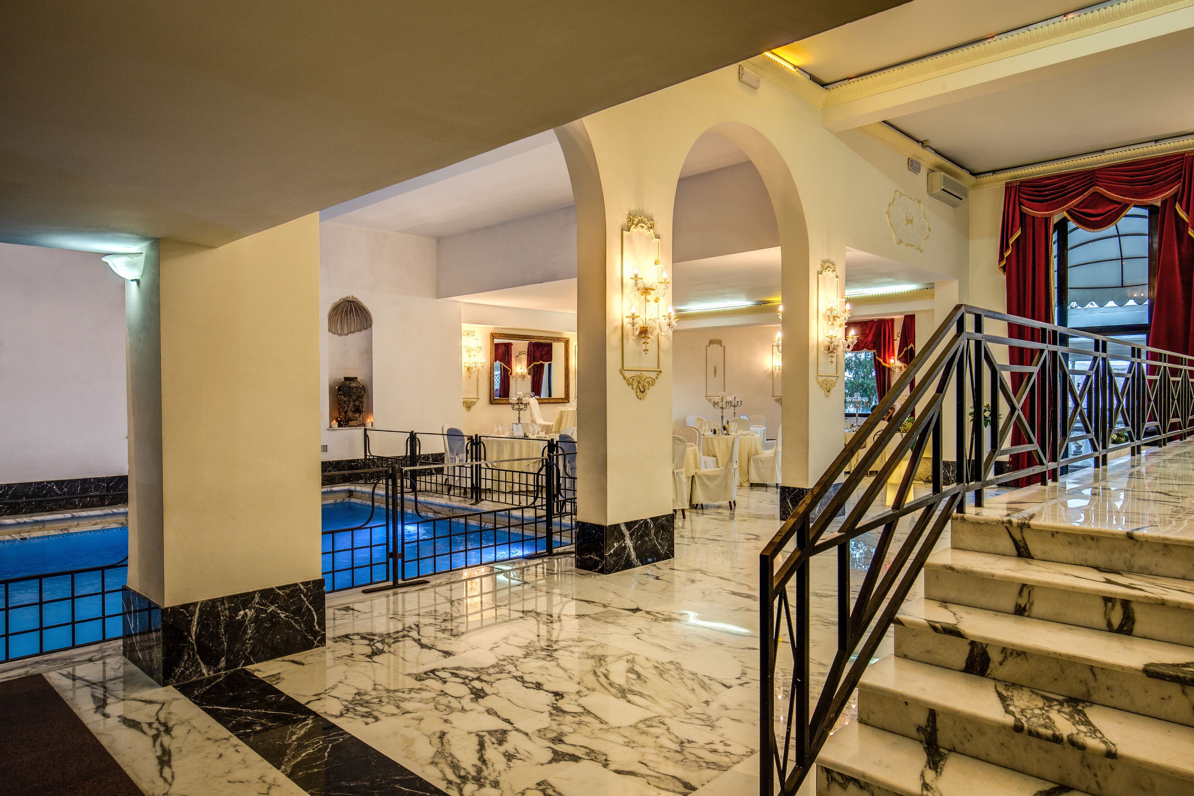 A hotel lobby with marble flooring, a pool area, and a staircase with a metal railing.