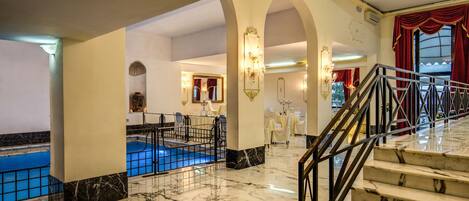 A hotel lobby with marble flooring, a pool area, and a staircase with a metal railing.