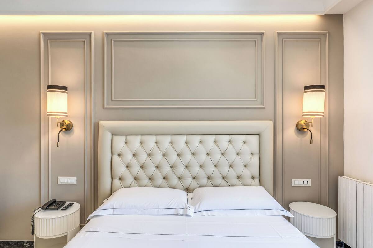 A hotel room with a tufted headboard, two bedside lamps, a round bedside table, and a telephone.