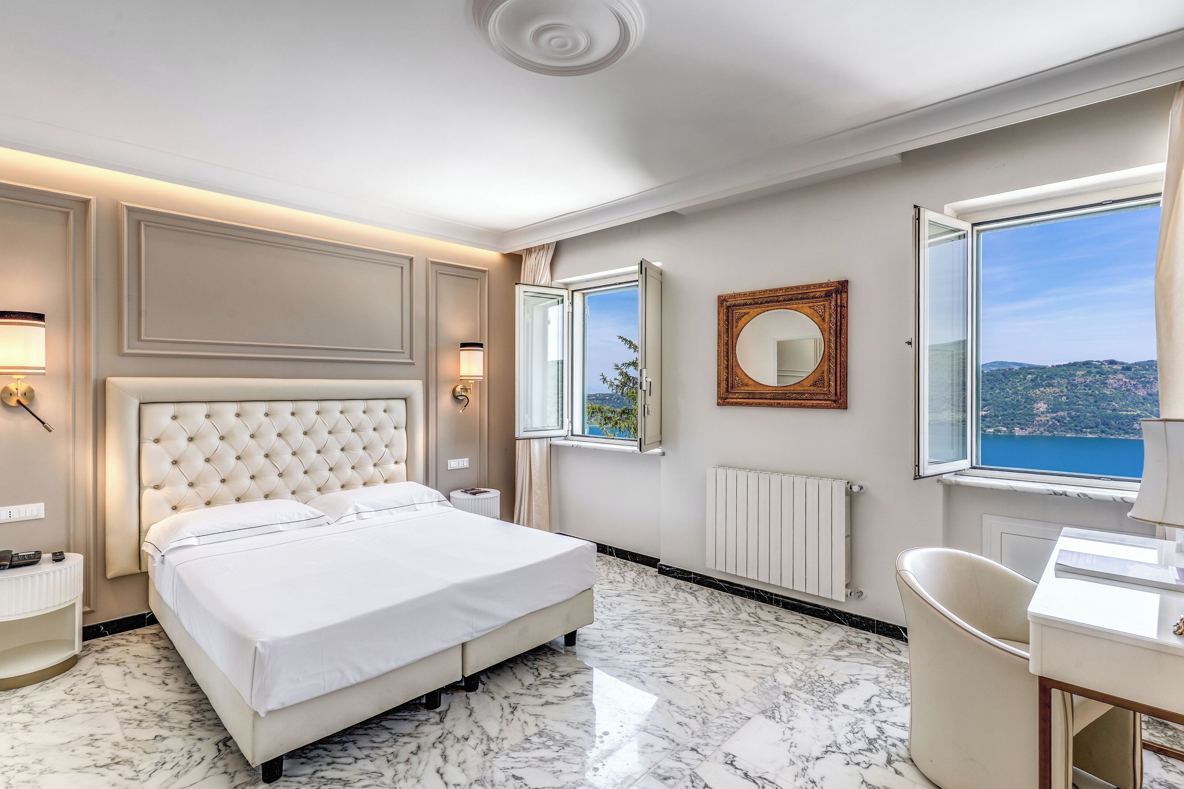 Ein Hotelzimmer mit einem großen Bett, einem Schreibtisch, einem Sessel, einem Fenster mit Ausblick und einem Spiegel an der Wand.