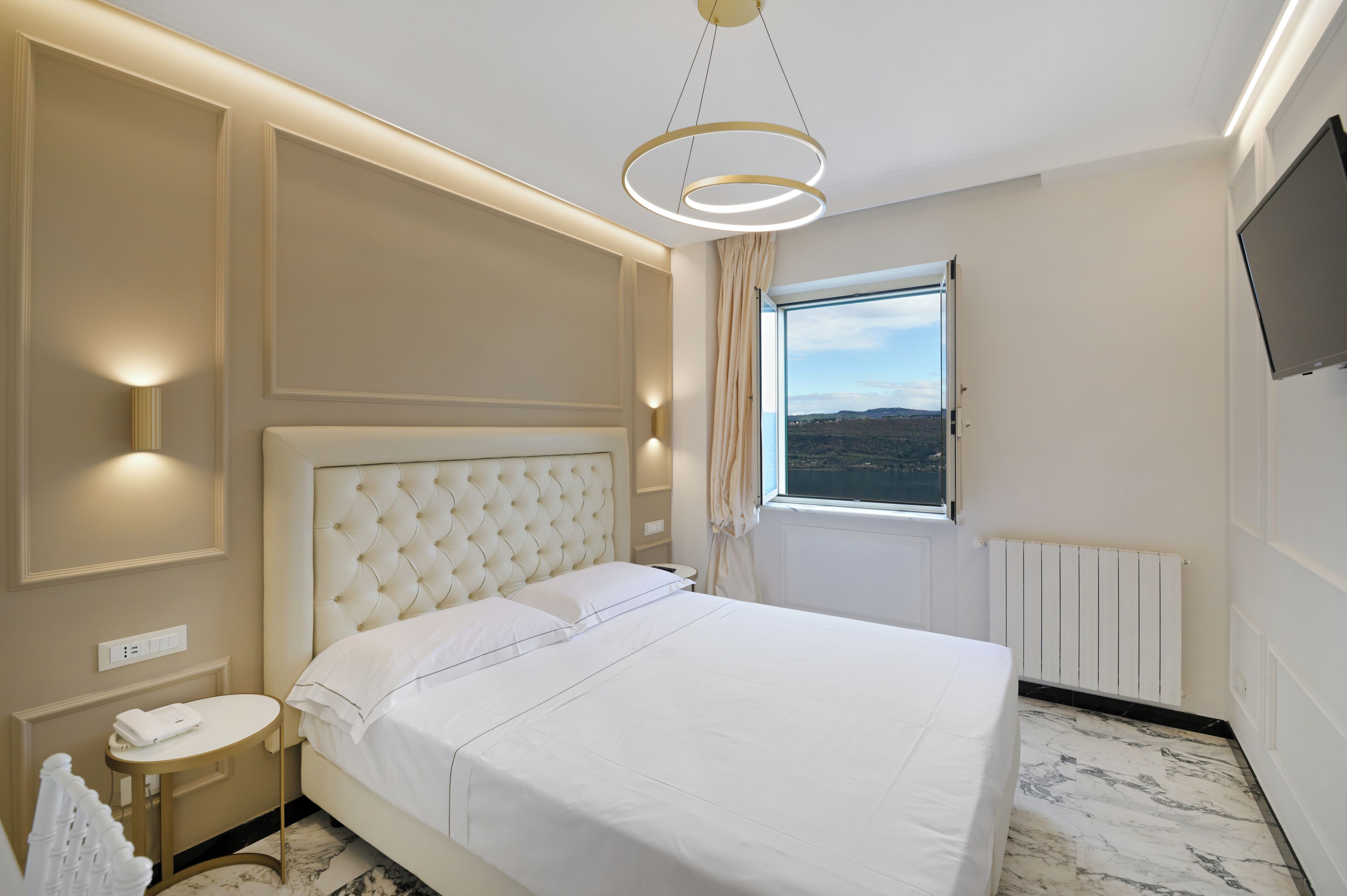 Quarto de hotel com uma cama grande, mesa de cabeceira, televisão e janela com vista.