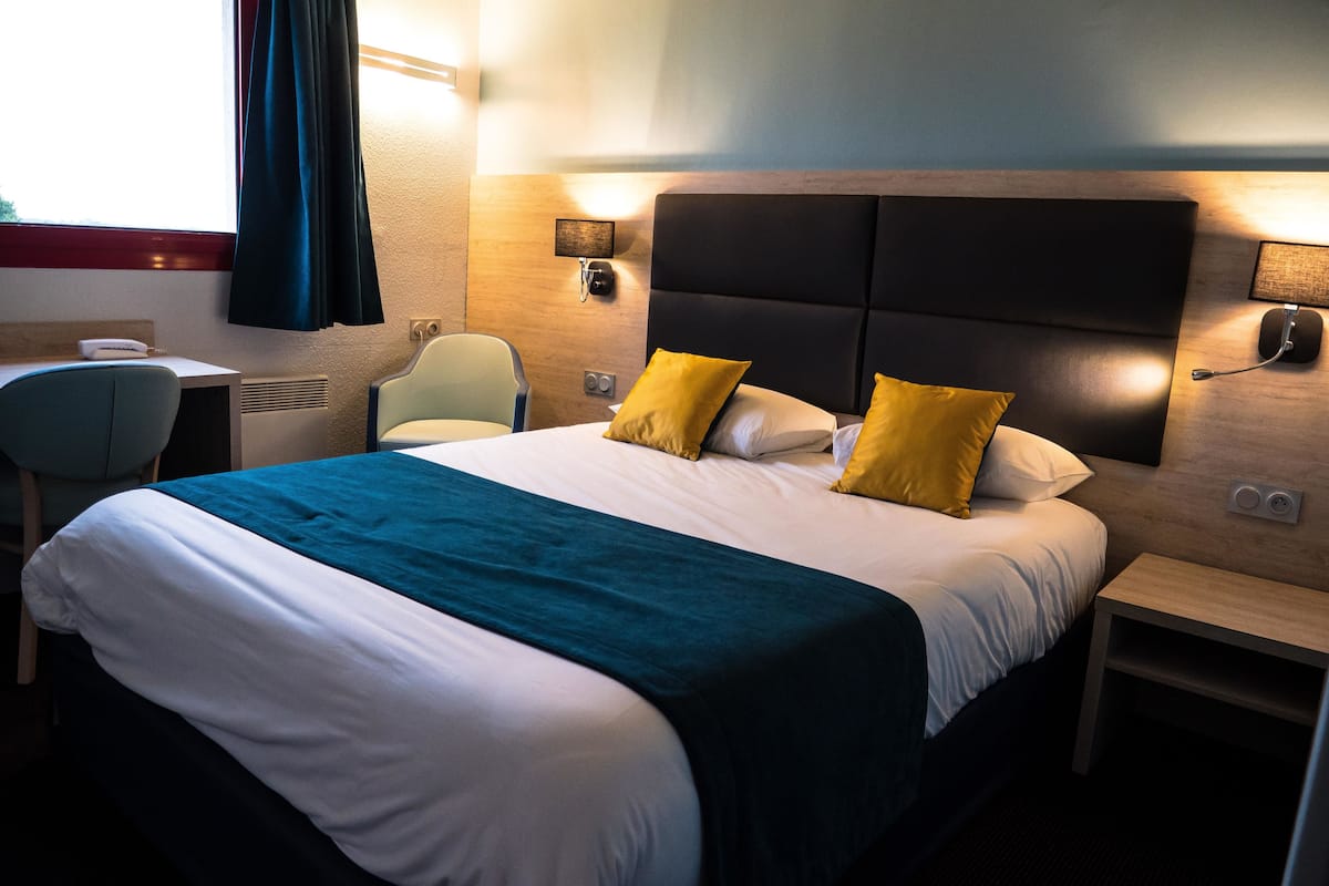 Habitación de hotel con una cama grande, dos mesitas de noche, un escritorio, una silla y una ventana con cortinas.