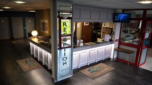 Un espace d’accueil comprenant un comptoir de réception, un écran numérique affichant un menu et une porte donnant accès à un restaurant.