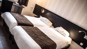 Deux lits simples avec une literie blanche et marron, un bureau avec un téléphone et un luminaire fixé au mur.
