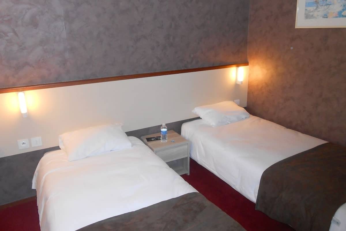 Habitación de hotel con dos camas, una mesita de noche con una botella de agua y una lámpara en la pared.
