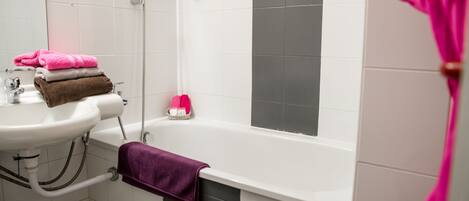 A bathroom with a white sink, a bathtub, and a shower. There are towels stacked on the sink and a purple towel hanging on the wall.